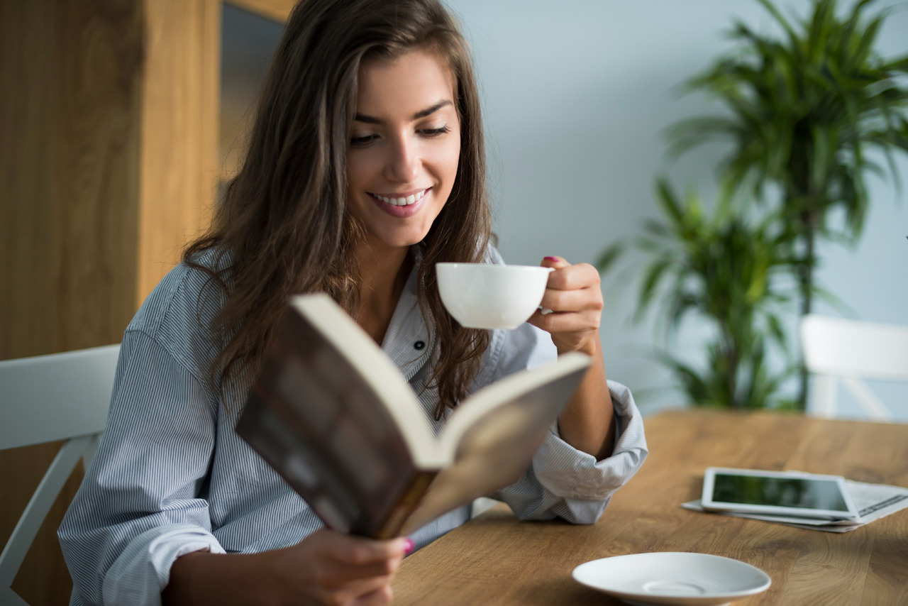 uma mulher lendo um livro com um café em mãos para simbolizar editoras de livros