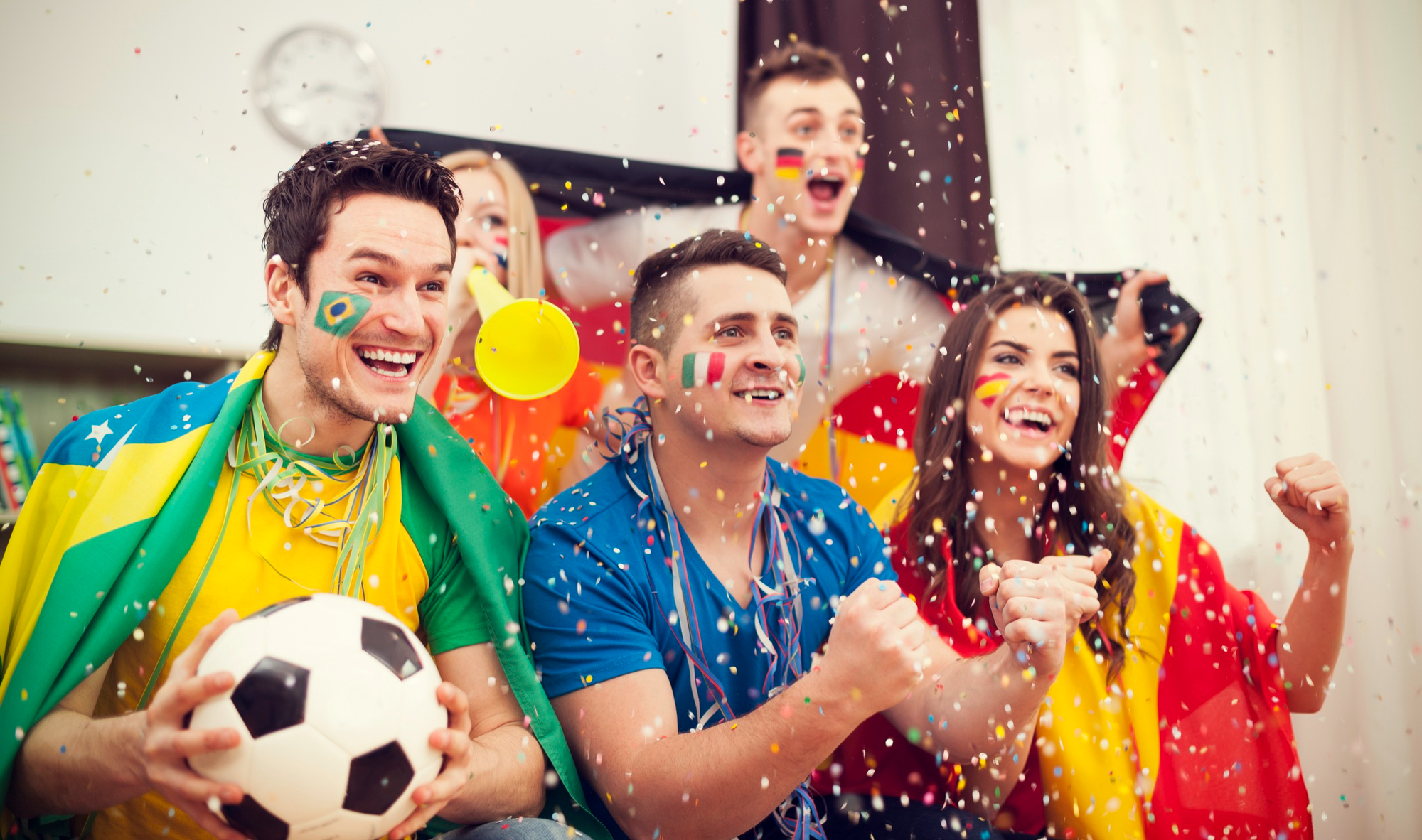 Imagem de várias pessoas vestidas e pintadas com coisas e cores de futebol, torcendo e vibrando para simbolizar o Dia Nacional do Futebol